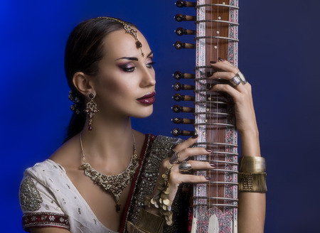 Beautiful Young Indian Woman in Traditional Sari Clothing with oriental jewelry, Bridal Makeup Playing the Sitar. Beautiful Bollywood Girl. Eastern fairy tale  (blue lens effect)の写真素材