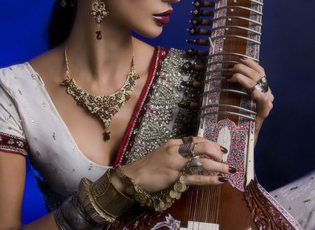 Beautiful Young Indian Woman in Traditional Sari Clothing with oriental jewelry, Bridal Makeup Playing the Sitar. Beautiful Bollywood Girl. Eastern fairy tale  (blue lens effect)の写真素材