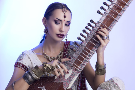 Beautiful Young Indian Woman in Traditional Sari Clothing with oriental jewelry, Bridal Makeup Playing the Sitar. Beautiful Bollywood Girl. Eastern fairy tale  (blue lens effect)の写真素材