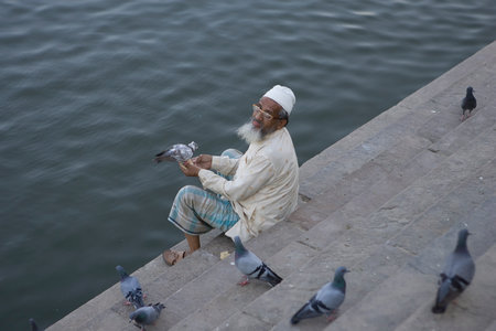 VARANASI, INDIA - MAY 15: Unidentified old man feeds pigeons near holy river Ganga May 15, 2013 in Varanasi, India. According to legend, Varanasi was founded by Lord Shiva.のeditorial素材