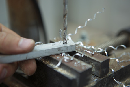 Man drilling in Steel Plate with Bench Drill. Close-up Electric drilling machine with manual pressure, a man holding a metal part and the hole is drilled, pressing drill to the workpiece surfaceの写真素材
