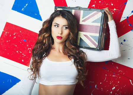 Beautiful Cute young Woman posing with a Suitcase. Young Woman standing with the UK flag in the background. A Trip to England in London, Travel and Study. English language learning conceptの写真素材