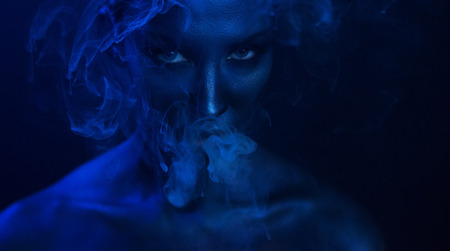 Halloween Vape Party, Nightlife. Beautiful Sexy Young Woman with glamorous mystical makeup vaping in...