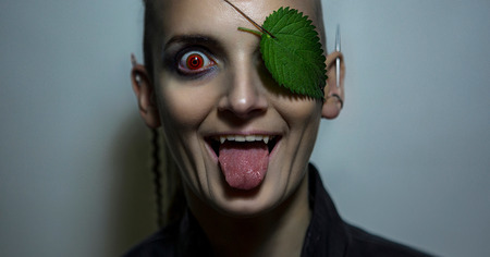 Portrait of an androgyne crazy model. Nature Protection. Model's Face with pale skin and green leaf...