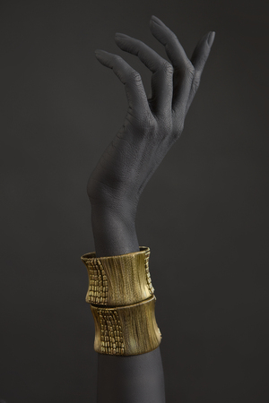Black woman's hand with gold jewelry. Oriental Bracelets on a black painted hand. Gold Jewelry and luxury accessories on black background closeup. High Fashion art concept の写真素材