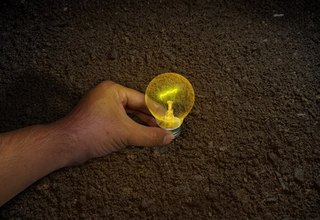 Human hand holding a light bulb on soil background, Energy saving concept.