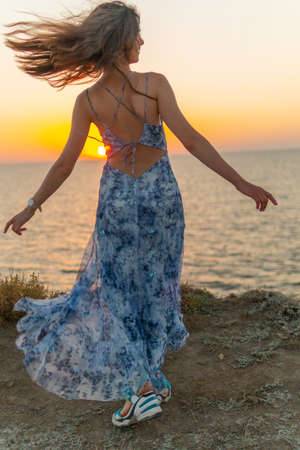 A girl in a long dress is spinning against the backdrop of a sunset in the summer at seaの写真素材