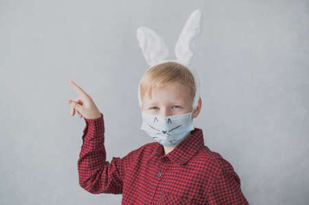 Boy with bunny ears wearing protective medical mask on a gray background. Easter holiday concept.の写真素材