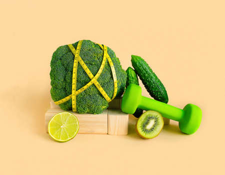Fresh green vegetables and fruits on a pastel background with dumbbells and measuring tape. Food balance, Equilibrium.Copy space. Vegetarian, alkaline food concept. Healthy food.Fitness dietの写真素材
