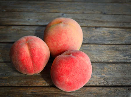Three ripe peaches on a vintage wooden table.の写真素材