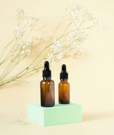 Dropper bottle. Bottle of dark glass on the podium with essential oil, care oil, hyaluronic acid,...
