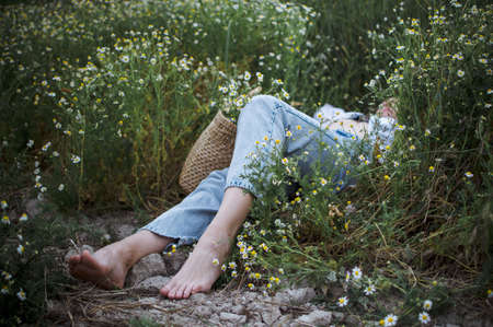 Young hipster woman lying on the field of daisies at sunset summer time. Lifestyle concept.