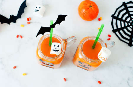 Drink for Halloween. hildrens and party of Halloween treats. Pumpkin orange cocktail in glasses, decorated with creepy faces scary marshmallows, bats, cobwebs on a white marble table. Copy space.の写真素材