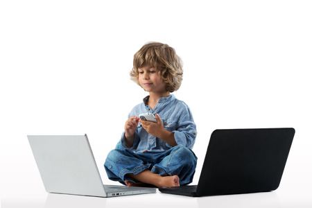 Little boy playing with a smart phote and two laptops
