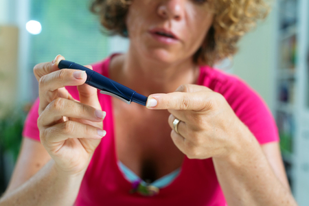 Close up of a female diabetic patient using lancelet on finger to take sample of blood sugar. の写真素材