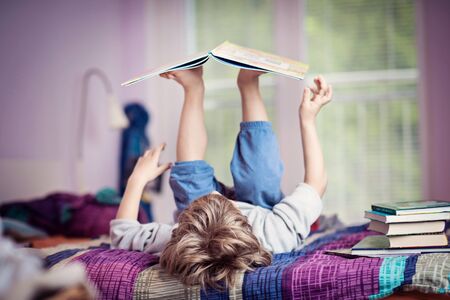 Little boy lying on bed playing with books.の写真素材