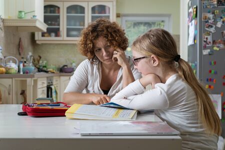 Mother helping daughter with her homework at the table in the dinning room.の写真素材