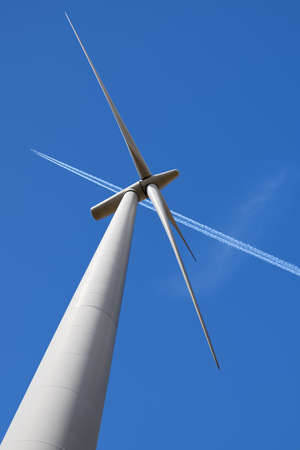 Wind Turbine and Aeroplane Vapour Trail Against a Blue Sky, United Kingdom. Low Angleの写真素材