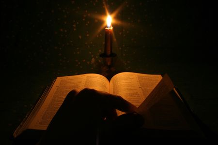 A bible open on a table next to a candleの写真素材