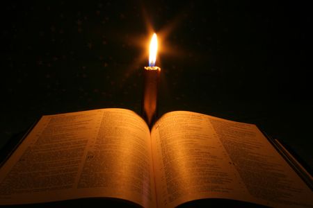 A bible open on a table next to a candleの写真素材
