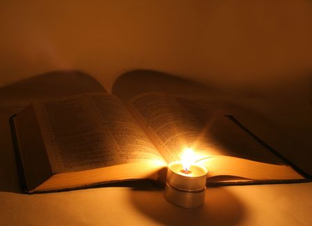 A bible open on a table next to a candleの写真素材