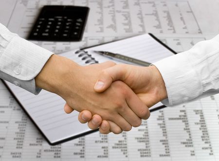 handshake over paper and pen,blurry computer in the backgroundの写真素材
