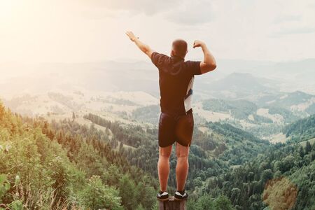 Man standing on of stump in summer mountains at sunset and enjoying view of natureの写真素材