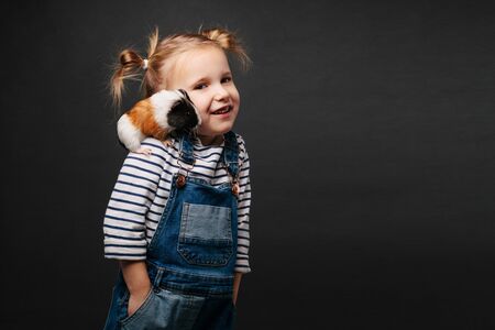 Girl holding a guinea pig in her arms, on a blackの写真素材