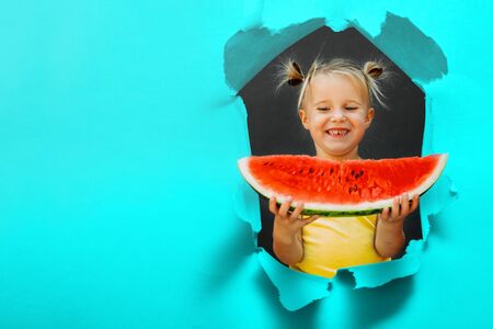 Funny kid eating watermelon outdoors on the gray backgrounds.  healthy food, girl. torn hole in paperの写真素材