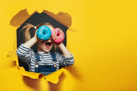 Happy cute boy is having fun played with donuts on Lush Lava background wall. Bright photo of a boy. Colored donutsの写真素材