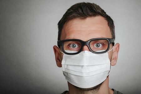 Face of a mask-wearing man with fear in the eye Close-up on a gray background.Coronavirus and Air...