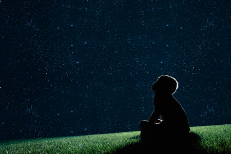 Ñchild sit on the grass at night and look at the night skyの写真素材