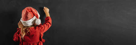 Girl in santa claus hat draws christmas drawing on the blackboardの写真素材