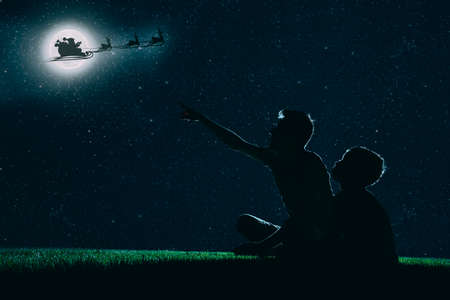 dad and son sit on the grass at night and look at the christmas night skyの写真素材