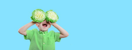 Happy cute boy is having fun played with green cabbage on yellow background wall.の写真素材