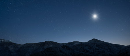 A star shines at night over the mountains.