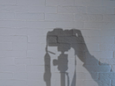 The shadow of a camera on a textured white brick wall. Stripes. The light from the lamp. Background.の写真素材