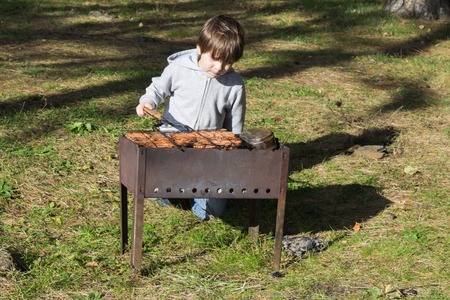 The boy fries meat on a brazierの写真素材