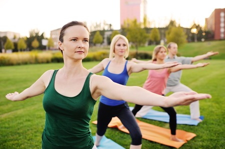 yoga group conducts training outdoors on a background of grass and sunsetの写真素材