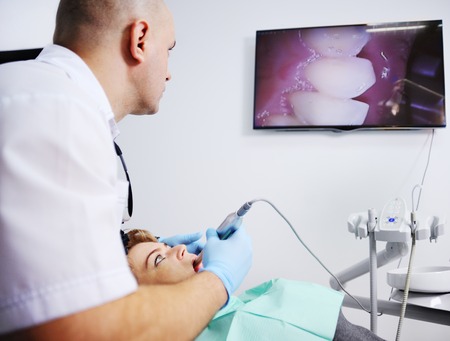 Male dentist examines a patient in the dental chair. Dentist patient shows his teeth on the big screenの写真素材