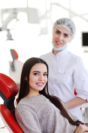 pretty young girl in red chair on the background of woman dentist smiling. Beautiful smile, whitening, modern clinicの写真素材