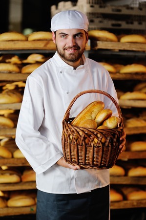 young handsome man holding a basket of baked goods on background bread storeの写真素材