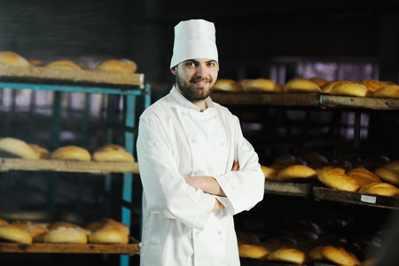 young handsome man baker in white uniform and cap on background bakeryの写真素材