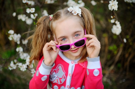 Baby girl in pink sunglasses against the background of blooming spring treesの写真素材