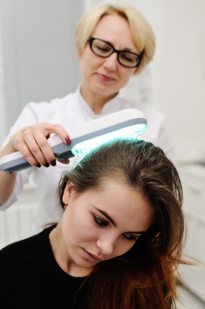 Doctor examines scalp a pretty young girl with special instrument UV lamp. Skin problems, dermatology, shingles, psoriasis, redness, preventionの写真素材