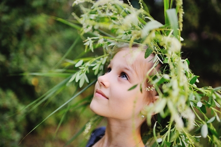 Baby girl in wreath of wild flowers and background of nature. A little girl looks at the sky and...