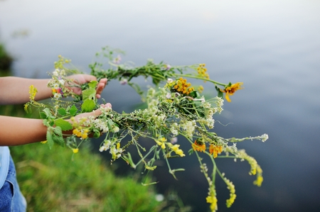 Wreath of wild flowers in childrens hands close-up on the background of the riverの写真素材