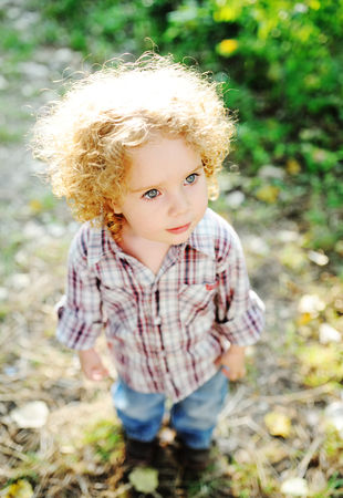 portrait of curly child on a background of green grass. On curly baby sun shines brightly.の写真素材