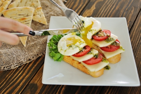 breakfast bread with egg poached, tomato, cheese and greens close-up on a wooden background