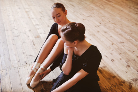 two ballerinas talking and smiling sitting on a wooden floor in a ballet classの写真素材